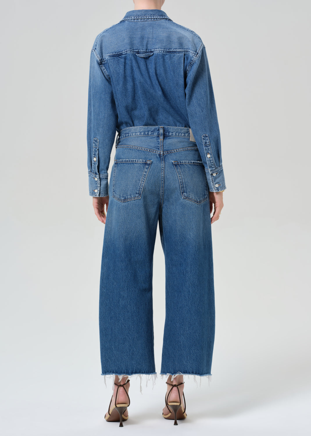 Person wearing a denim shirt with cropped jeans on a grey background