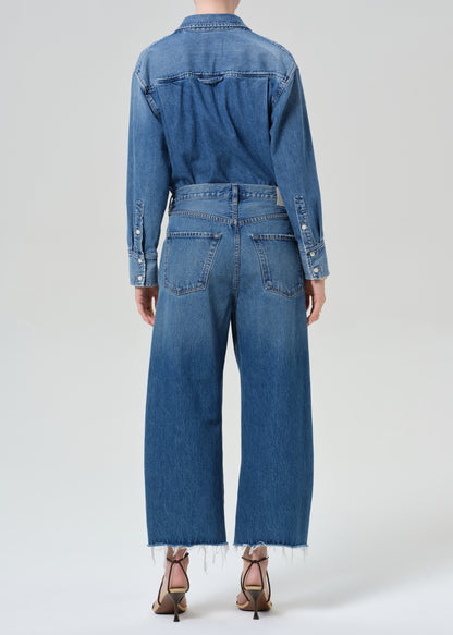 Person wearing a denim shirt with cropped jeans on a grey background