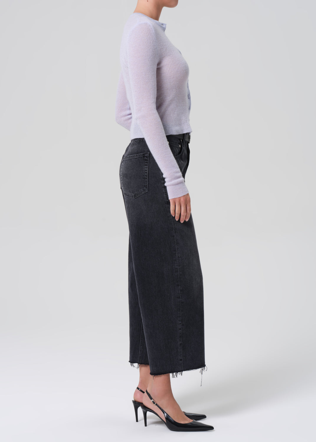 Person wearing a light blue long-sleeve top and black wide-leg jeans on a white background