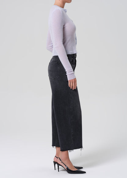 Person wearing a light blue long-sleeve top and black wide-leg jeans on a white background