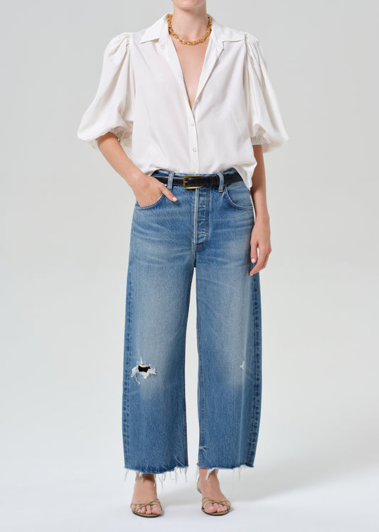 Person wearing a white blouse and blue jeans on a plain background