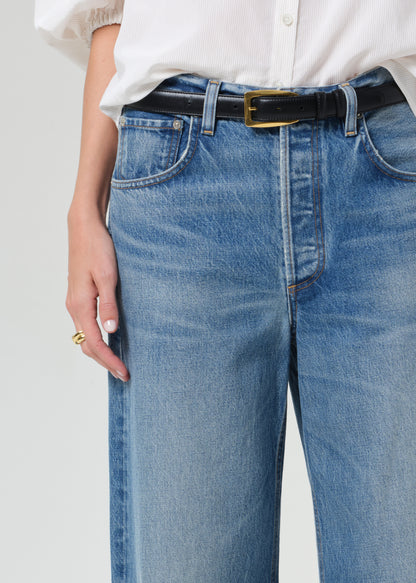 Person wearing blue jeans with a white shirt and black belt on a light gray background