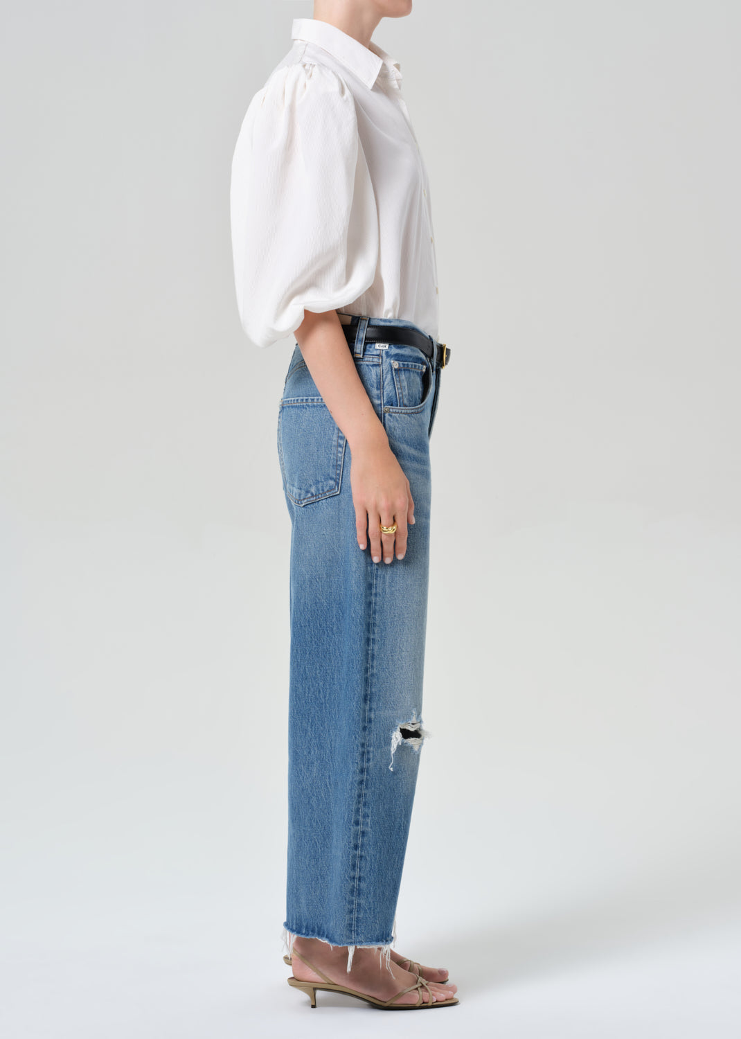 Person wearing a white blouse and blue jeans on a plain background