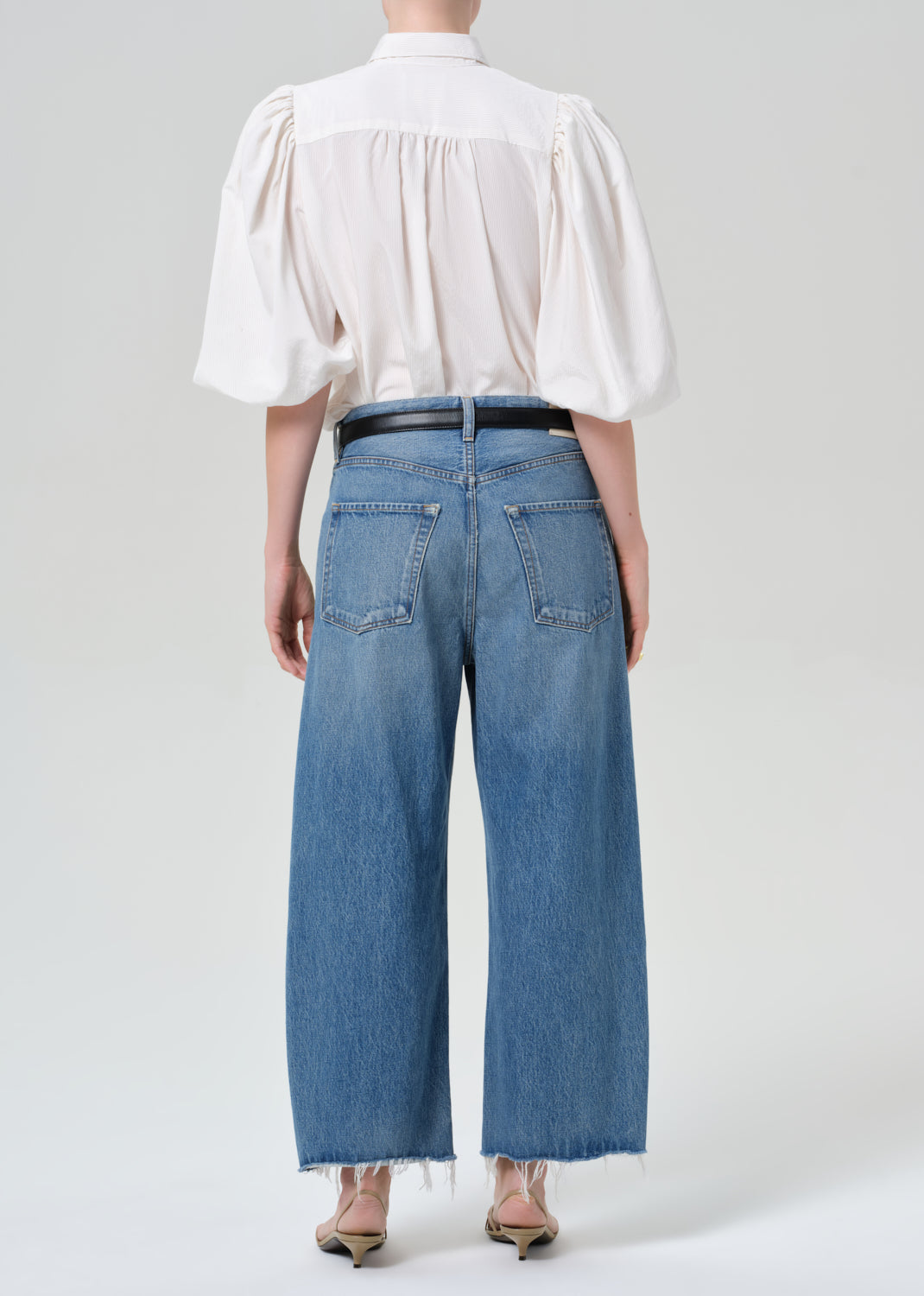 Person wearing a white blouse and blue jeans on a plain background