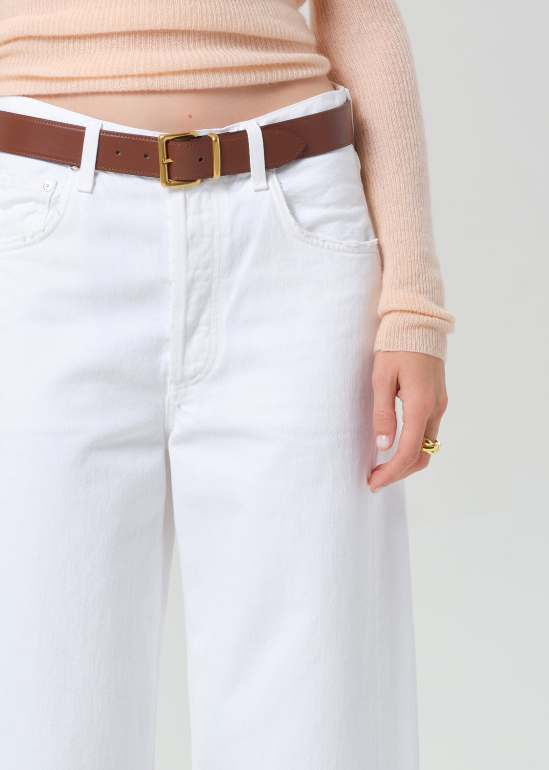 Person wearing a peach long-sleeve top and white jeans on a light gray background