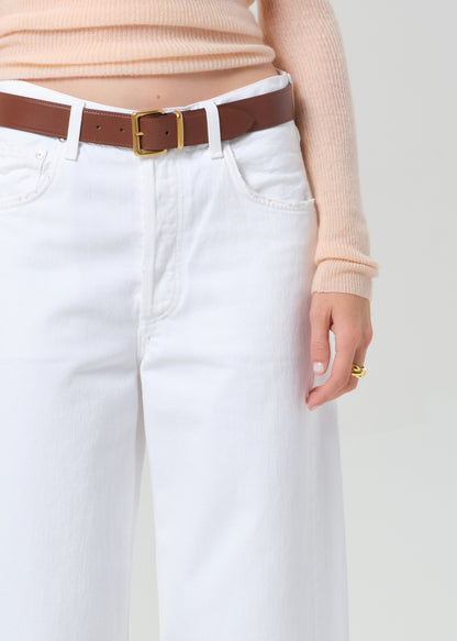 Person wearing a peach long-sleeve top and white jeans on a light gray background