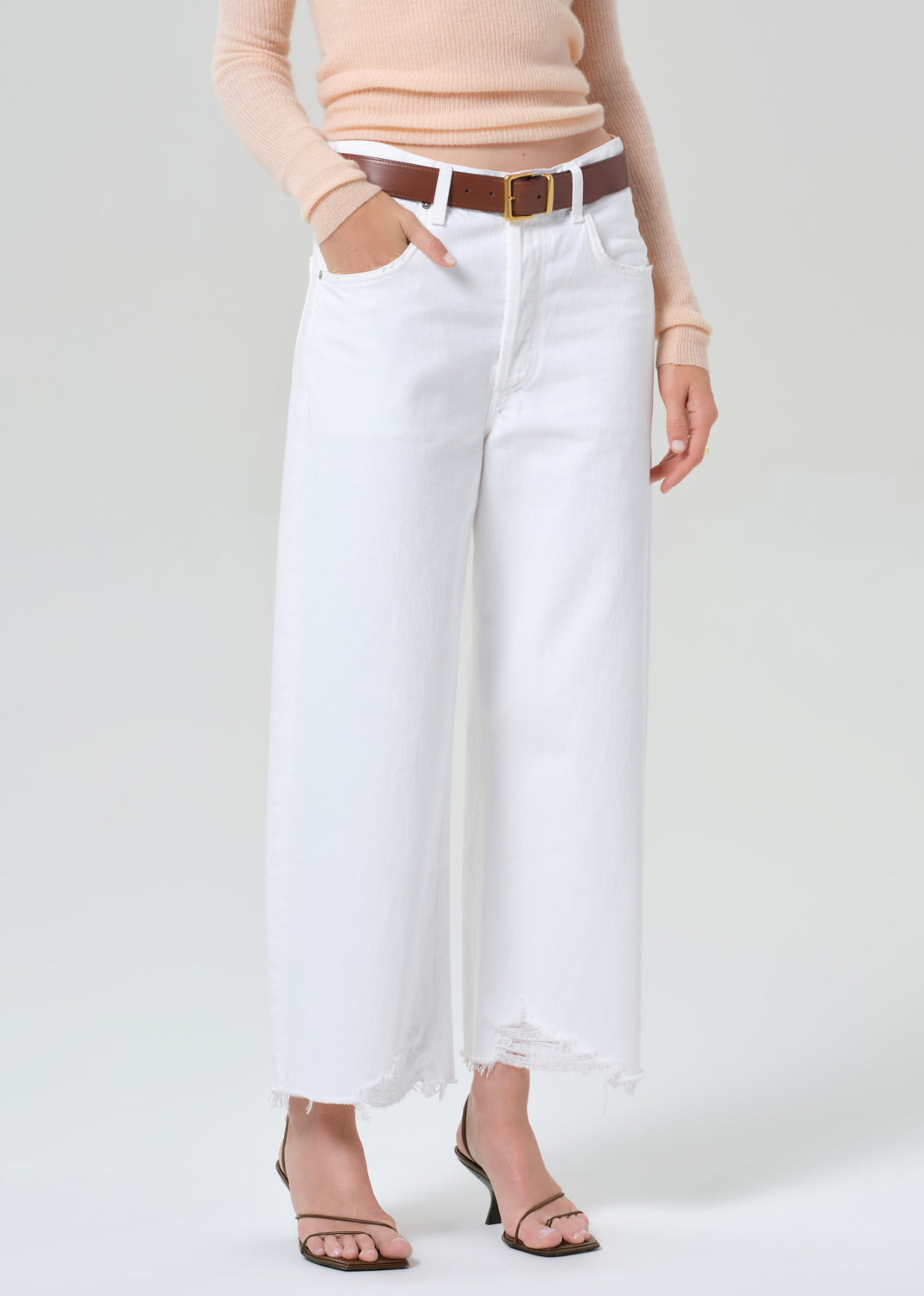 Person wearing a peach long-sleeve top and white jeans on a light gray background