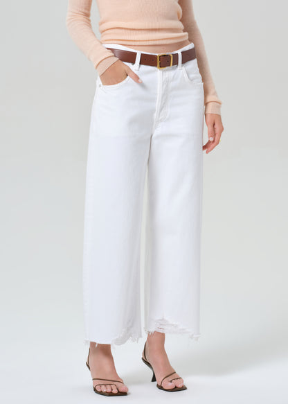 Person wearing a peach long-sleeve top and white jeans on a light gray background