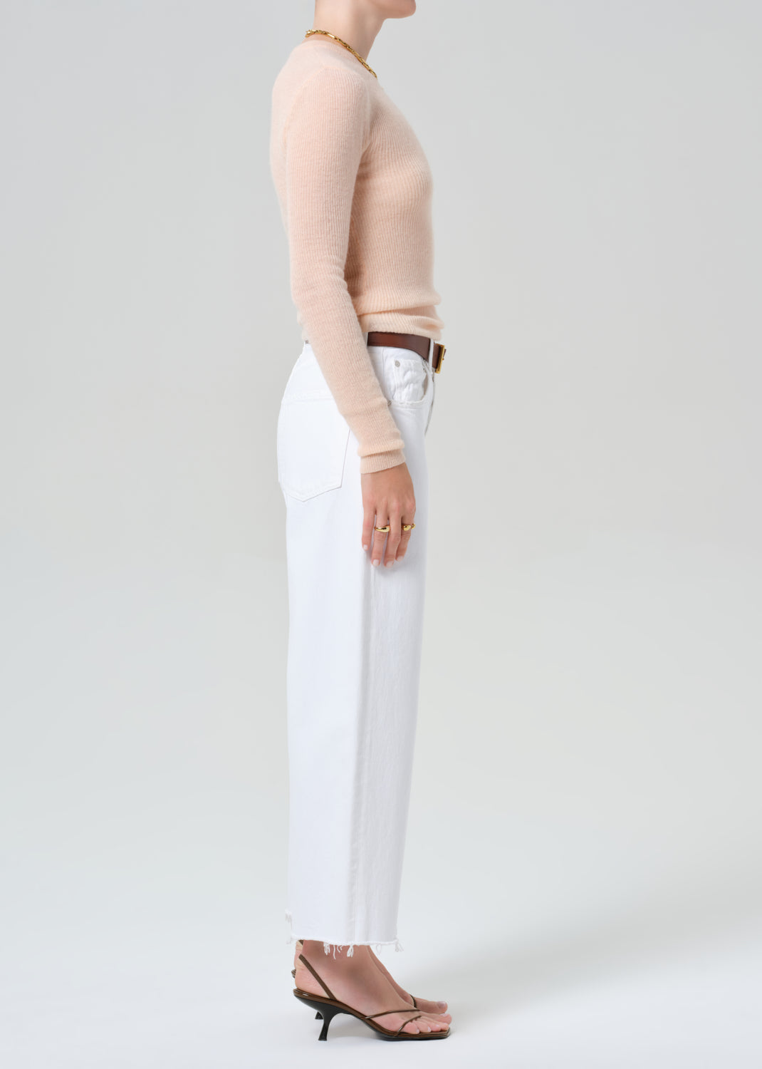 Person wearing a peach long-sleeve top and white jeans on a light gray background