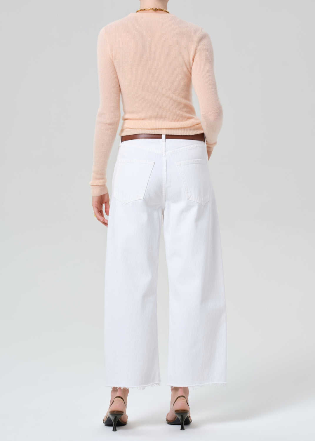 Person wearing a peach long-sleeve top and white jeans on a light gray background