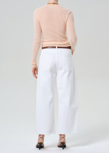 Person wearing a peach long-sleeve top and white jeans on a light gray background