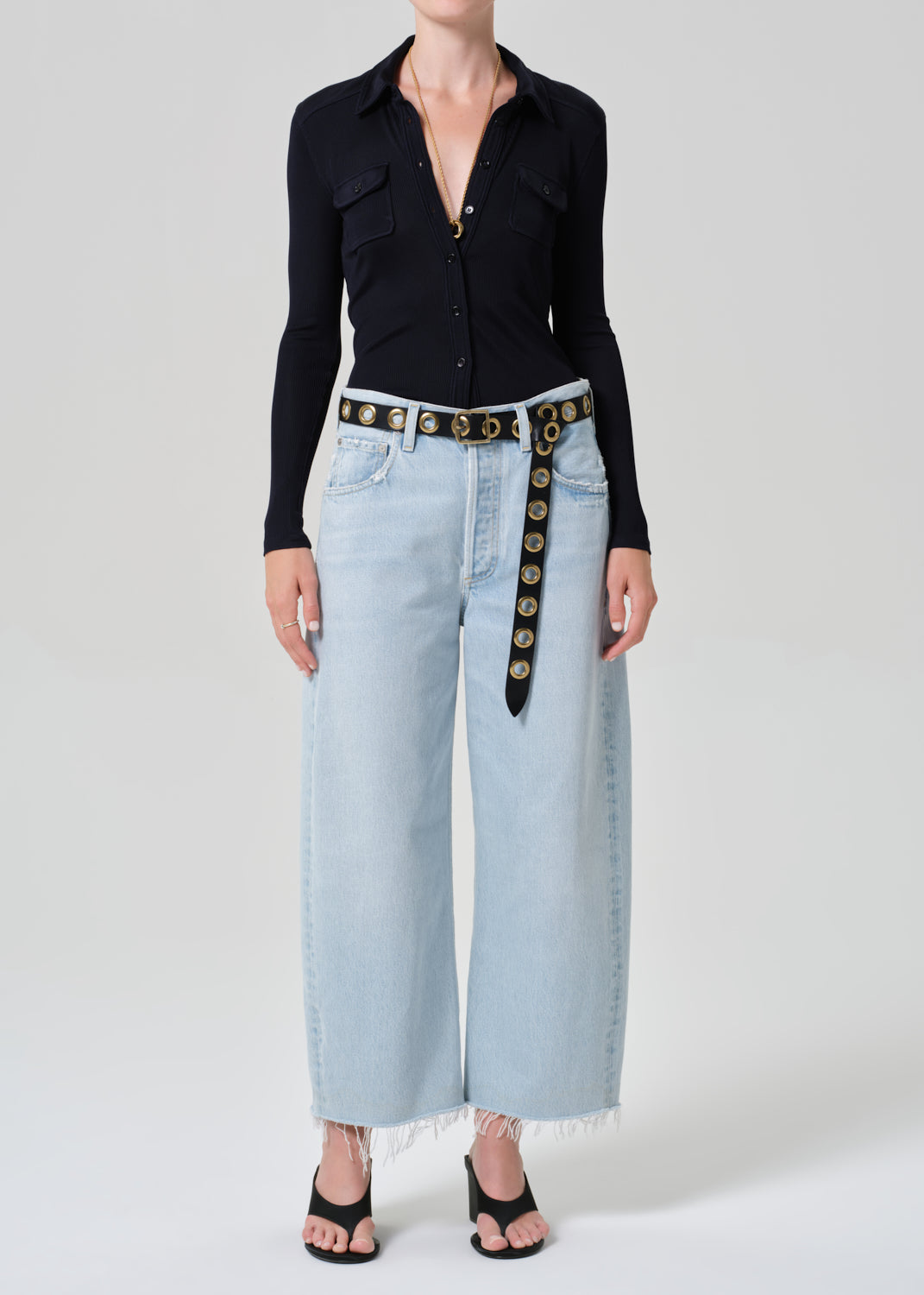 Person wearing a navy shirt and light blue jeans with a decorative belt on a plain background