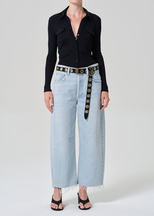 Person wearing a navy shirt and light blue jeans with a decorative belt on a plain background