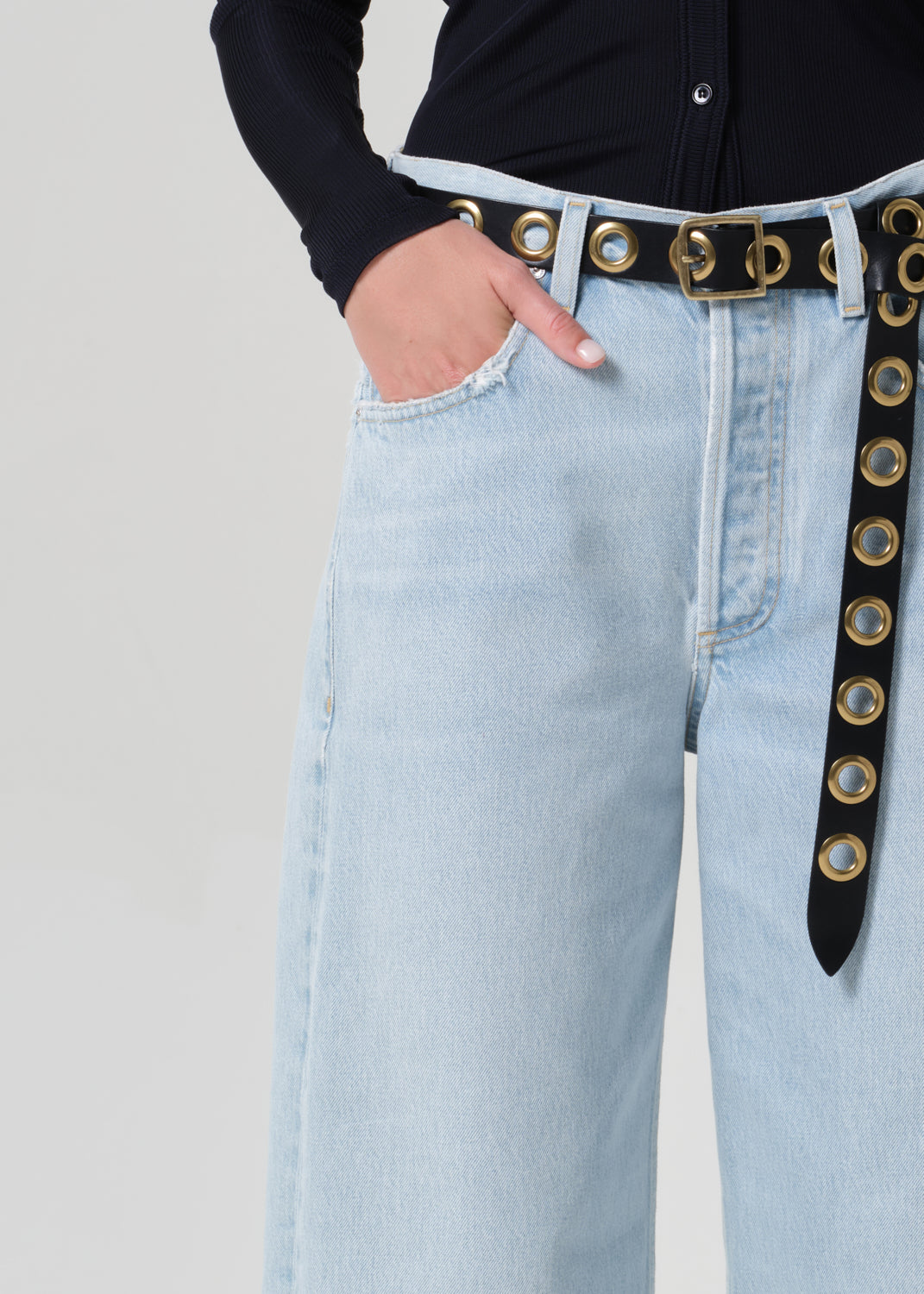 Person wearing a navy shirt and light blue jeans with a decorative belt on a plain background