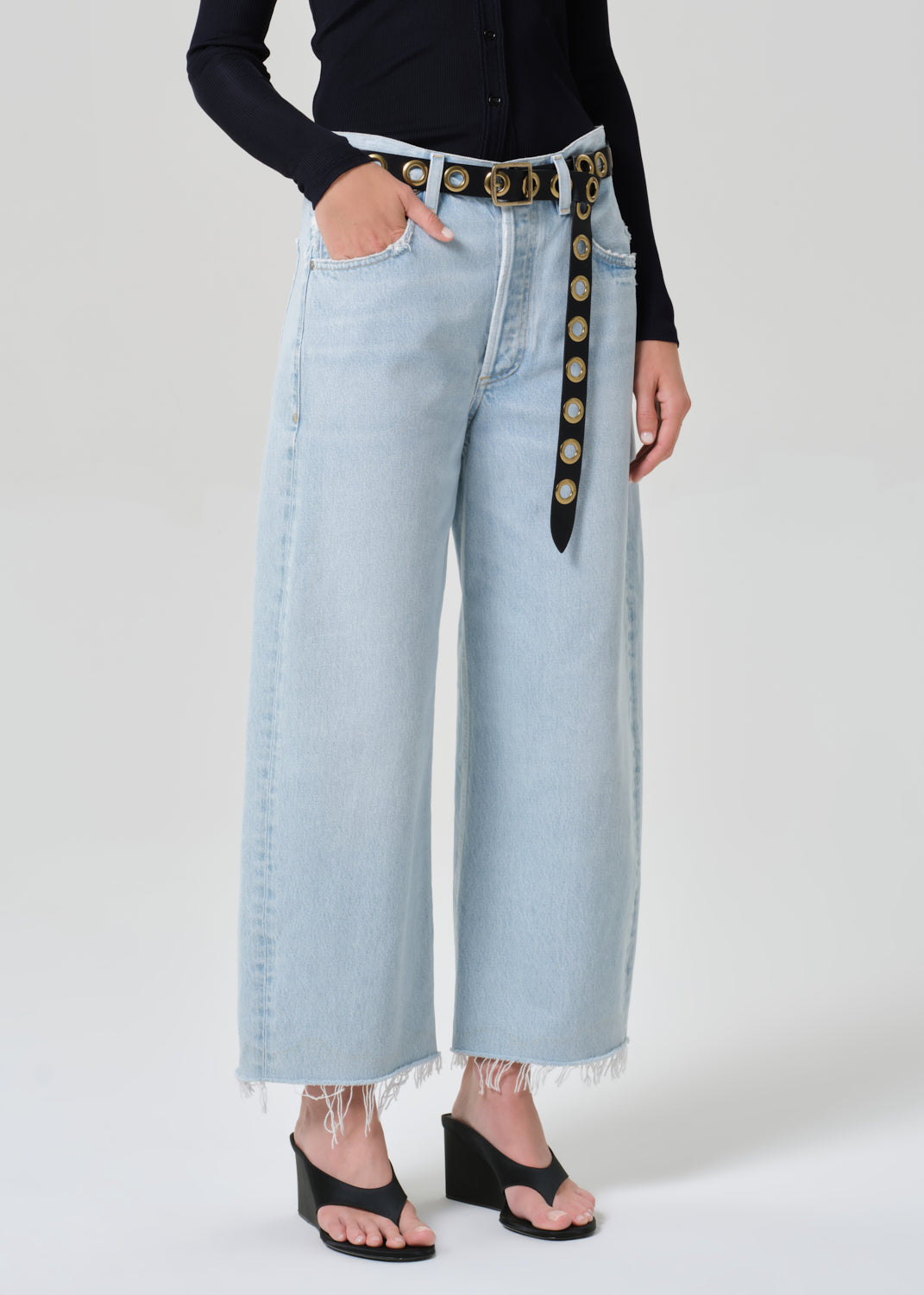 Person wearing a navy shirt and light blue jeans with a decorative belt on a plain background