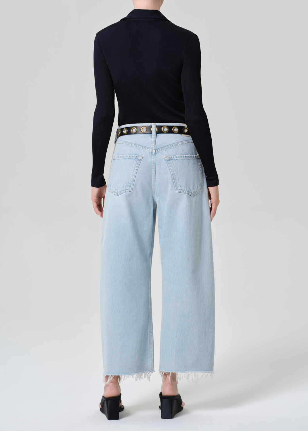 Person wearing a navy shirt and light blue jeans with a decorative belt on a plain background