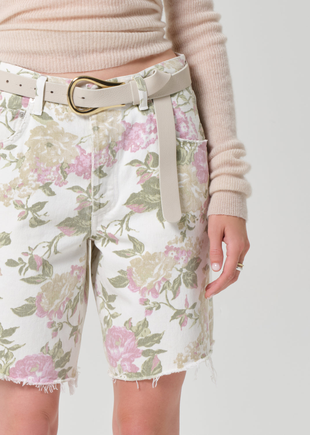 Person wearing a cream sweater and floral denim shorts on a grey background