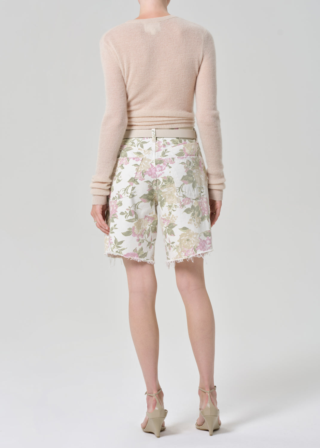 Person wearing a cream sweater and floral denim shorts on a grey background