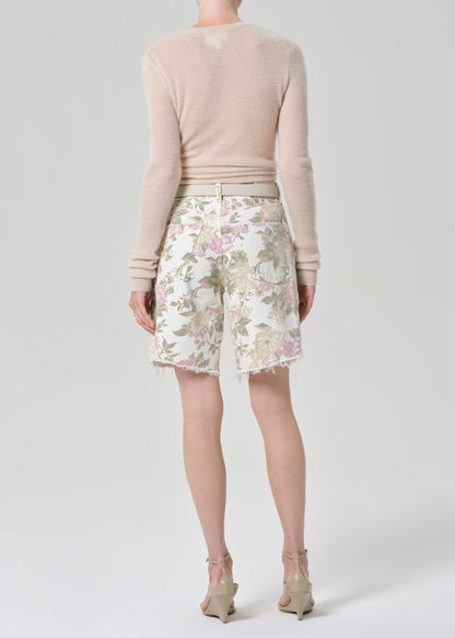 Person wearing a cream sweater and floral denim shorts on a grey background