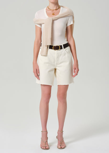 Person wearing a white top, CREAM cardigan, and white shorts on a plain background