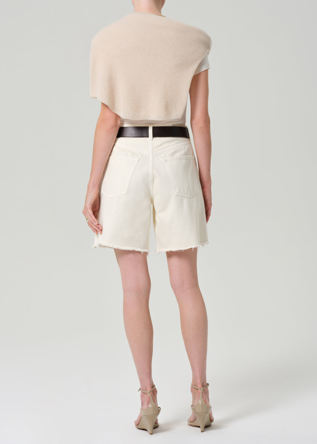 Person wearing a white top, CREAM cardigan, and white shorts on a plain background