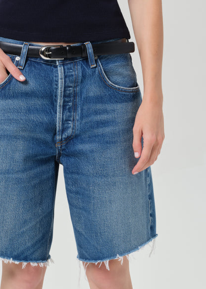 Person wearing a navy t-shirt and blue denim shorts on a grey background