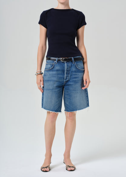 Person wearing a navy t-shirt and blue denim shorts on a grey background