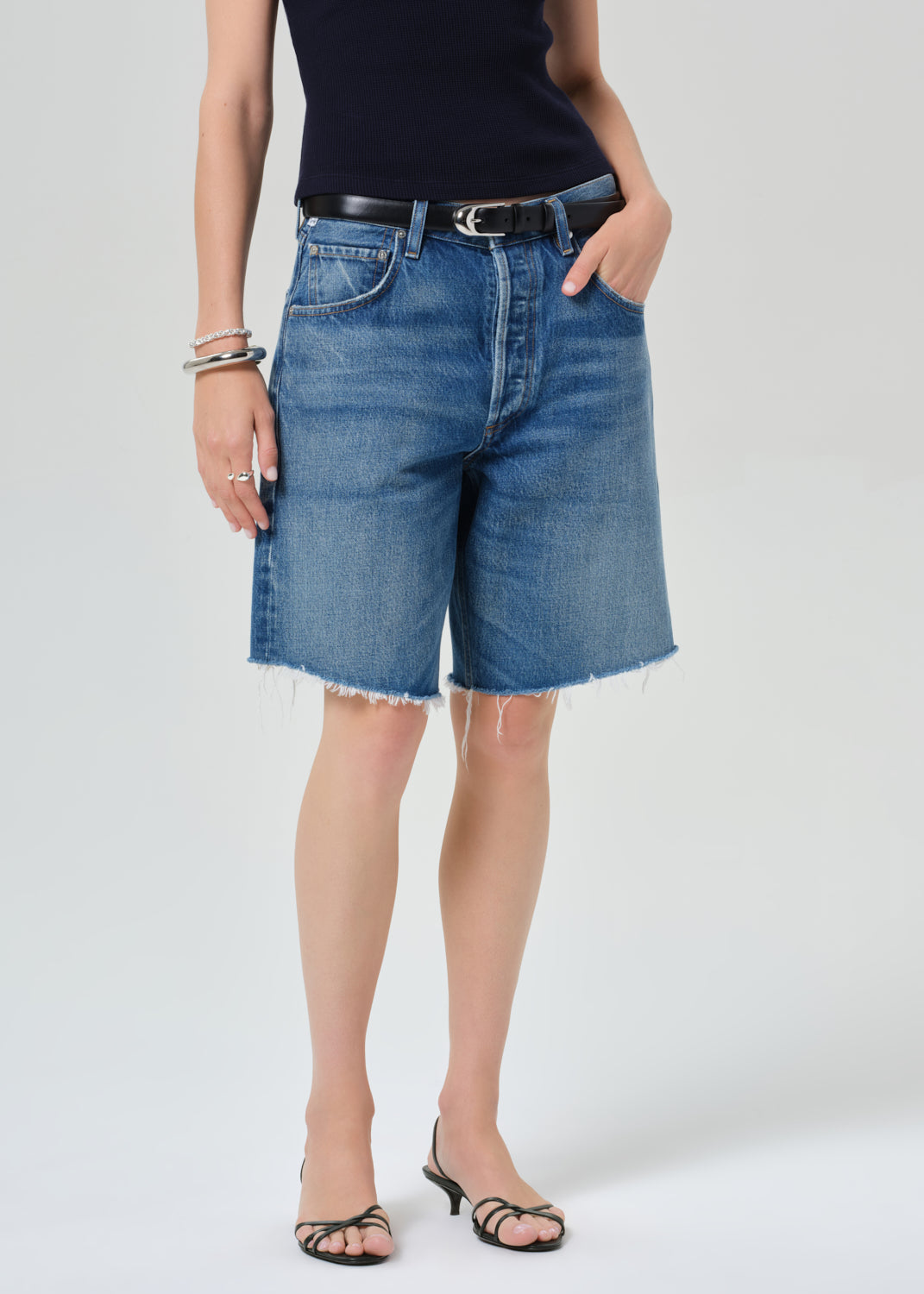 Person wearing a navy t-shirt and blue denim shorts on a grey background