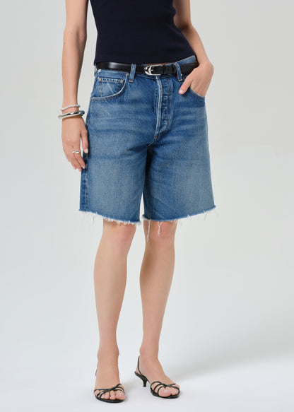 Person wearing a navy t-shirt and blue denim shorts on a grey background