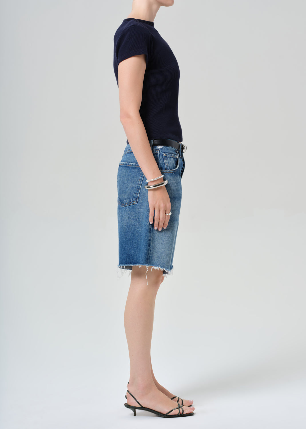 Person wearing a navy t-shirt and blue denim shorts on a grey background