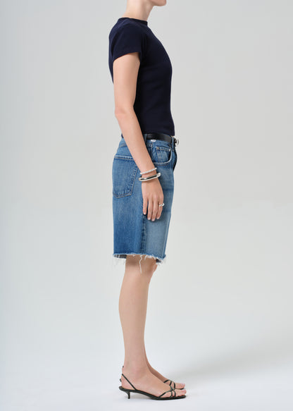 Person wearing a navy t-shirt and blue denim shorts on a grey background
