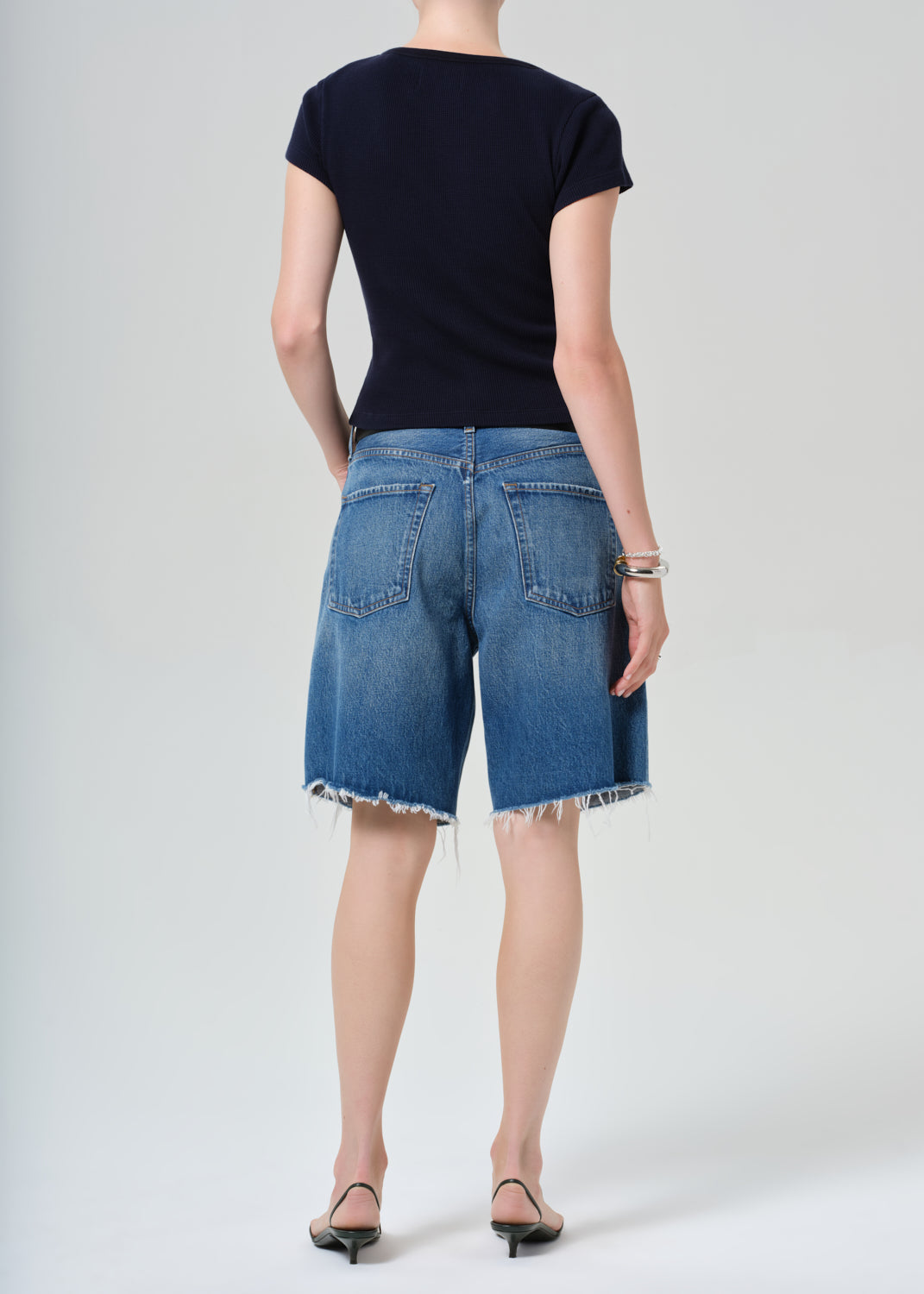 Person wearing a navy t-shirt and blue denim shorts on a grey background