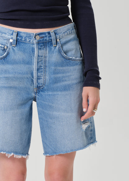 Person wearing a navy long-sleeve top and denim shorts on a grey background