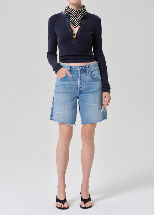 Person wearing a navy long-sleeve top and denim shorts on a grey background
