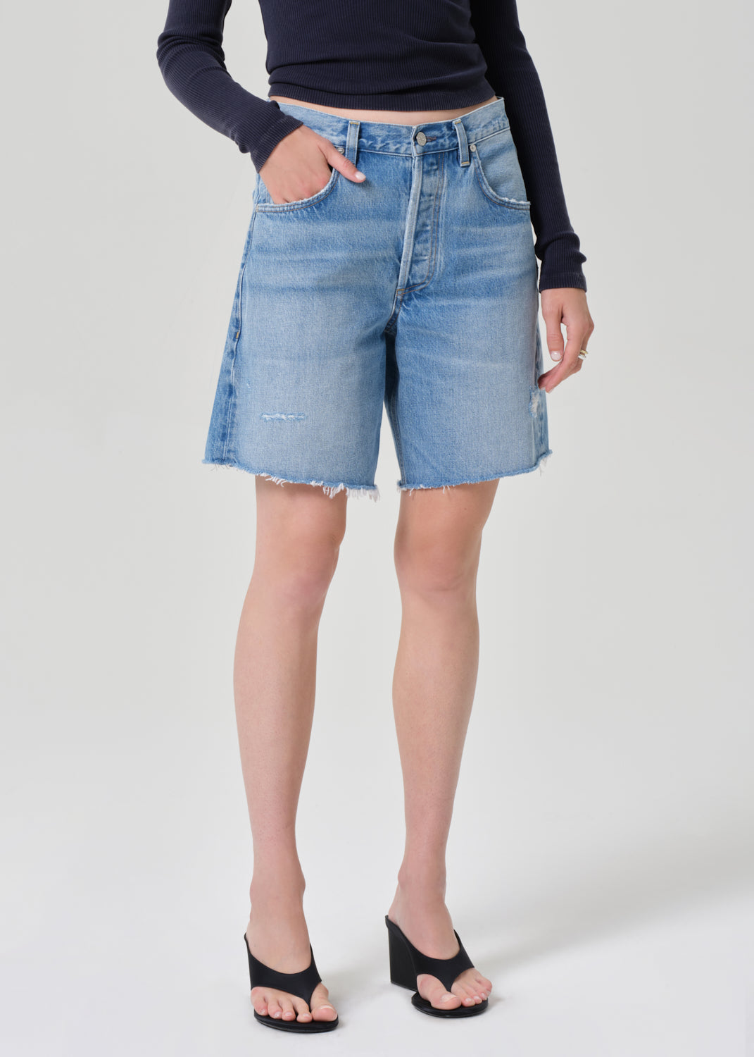 Person wearing a navy long-sleeve top and denim shorts on a grey background