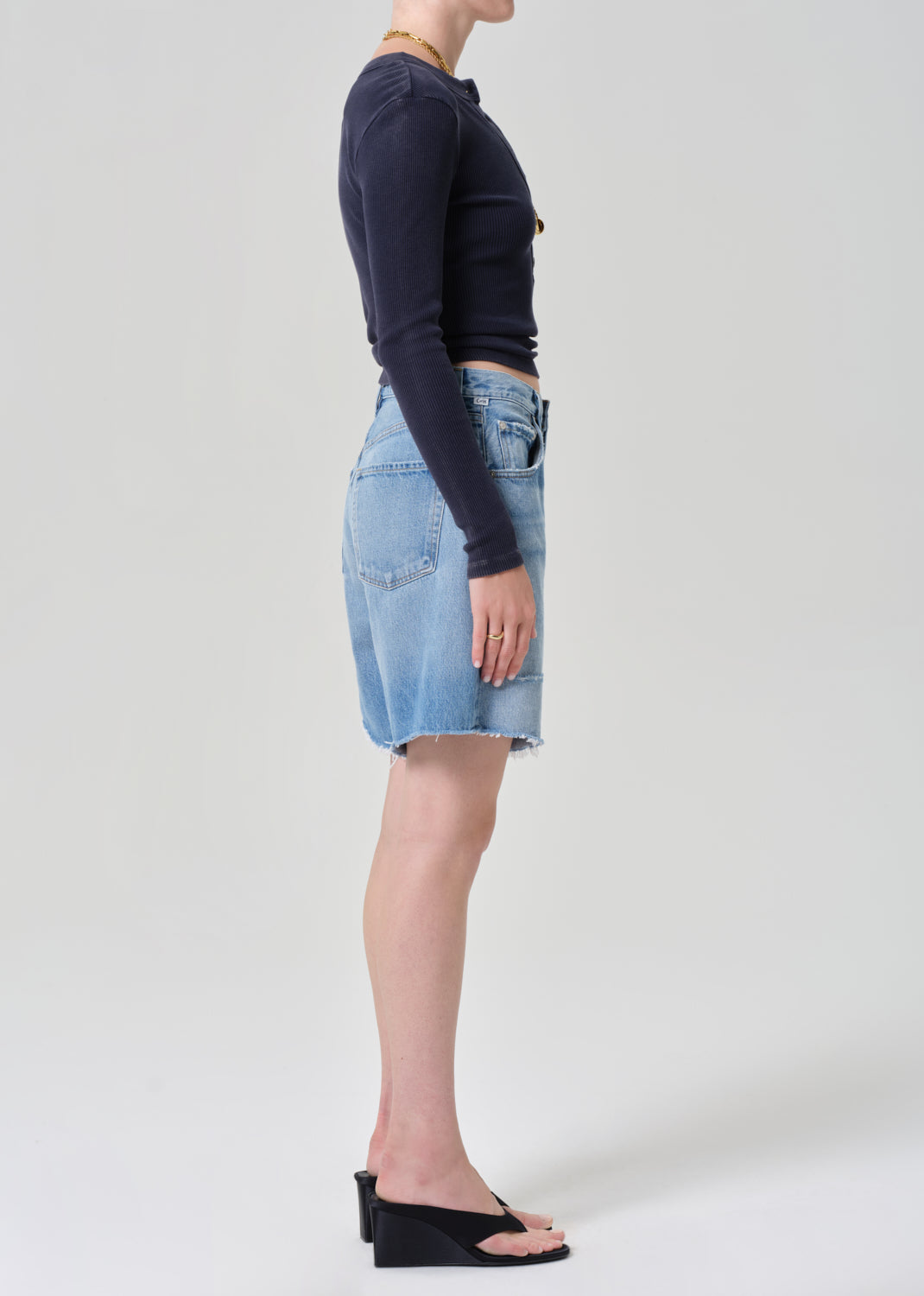 Person wearing a navy long-sleeve top and denim shorts on a grey background