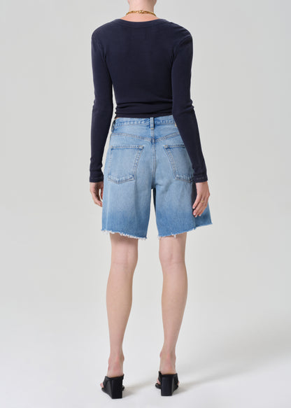 Person wearing a navy long-sleeve top and denim shorts on a grey background