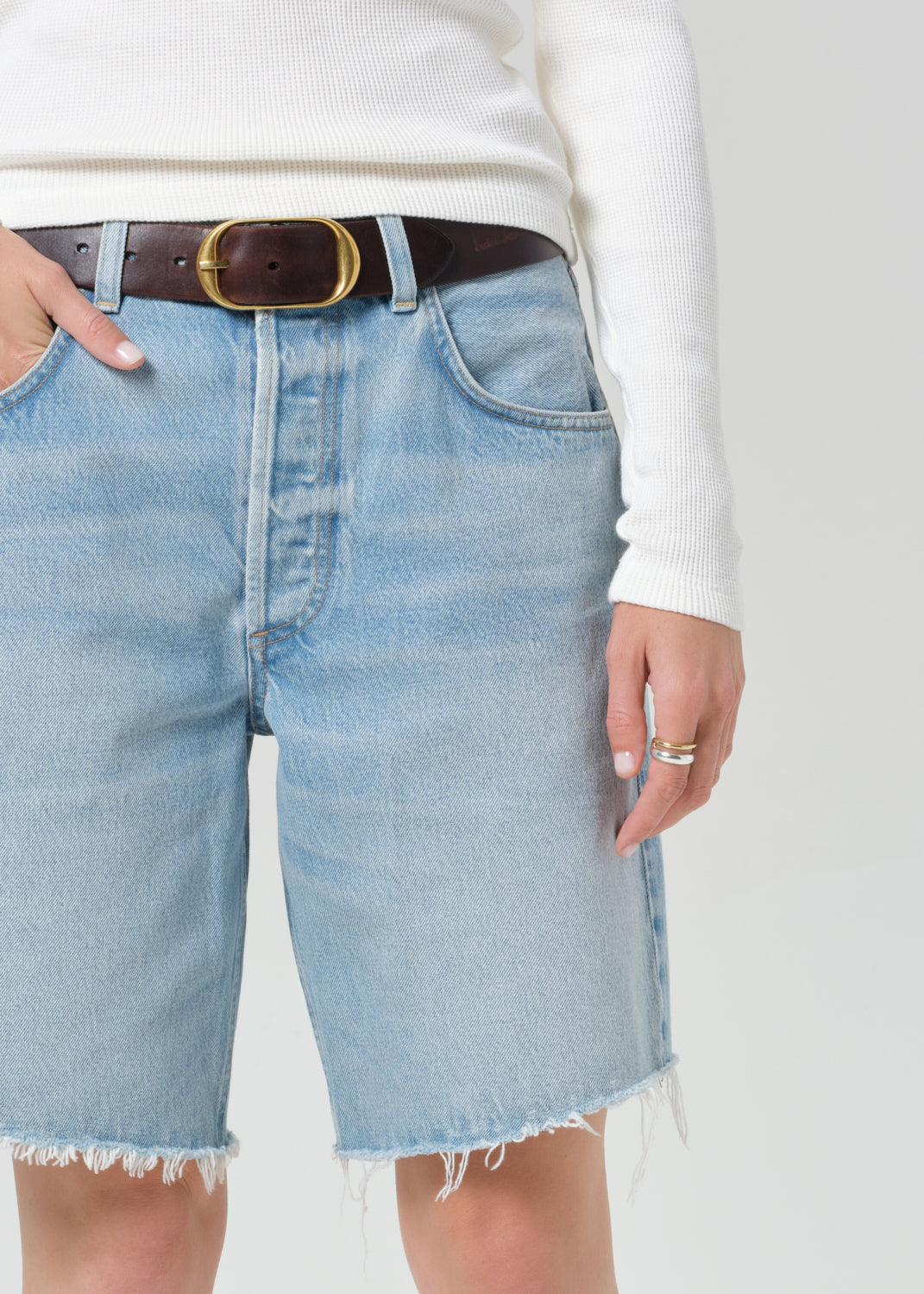 Person wearing a white long-sleeve shirt and light blue denim shorts on a plain background