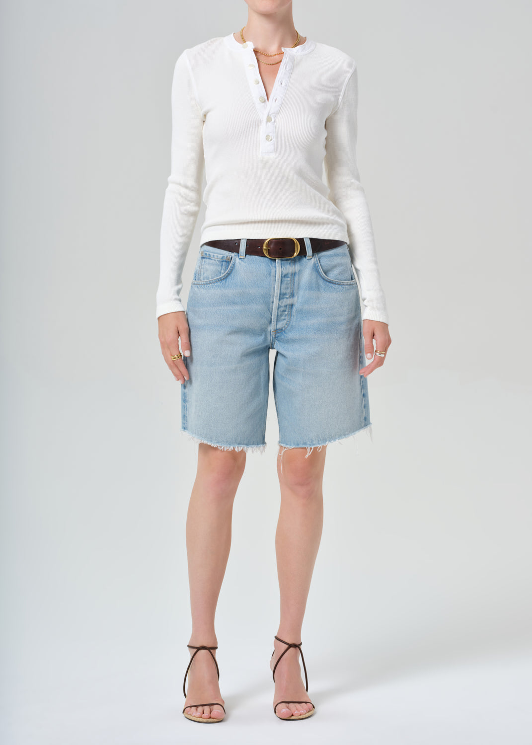 Person wearing a white long-sleeve shirt and light blue denim shorts on a plain background