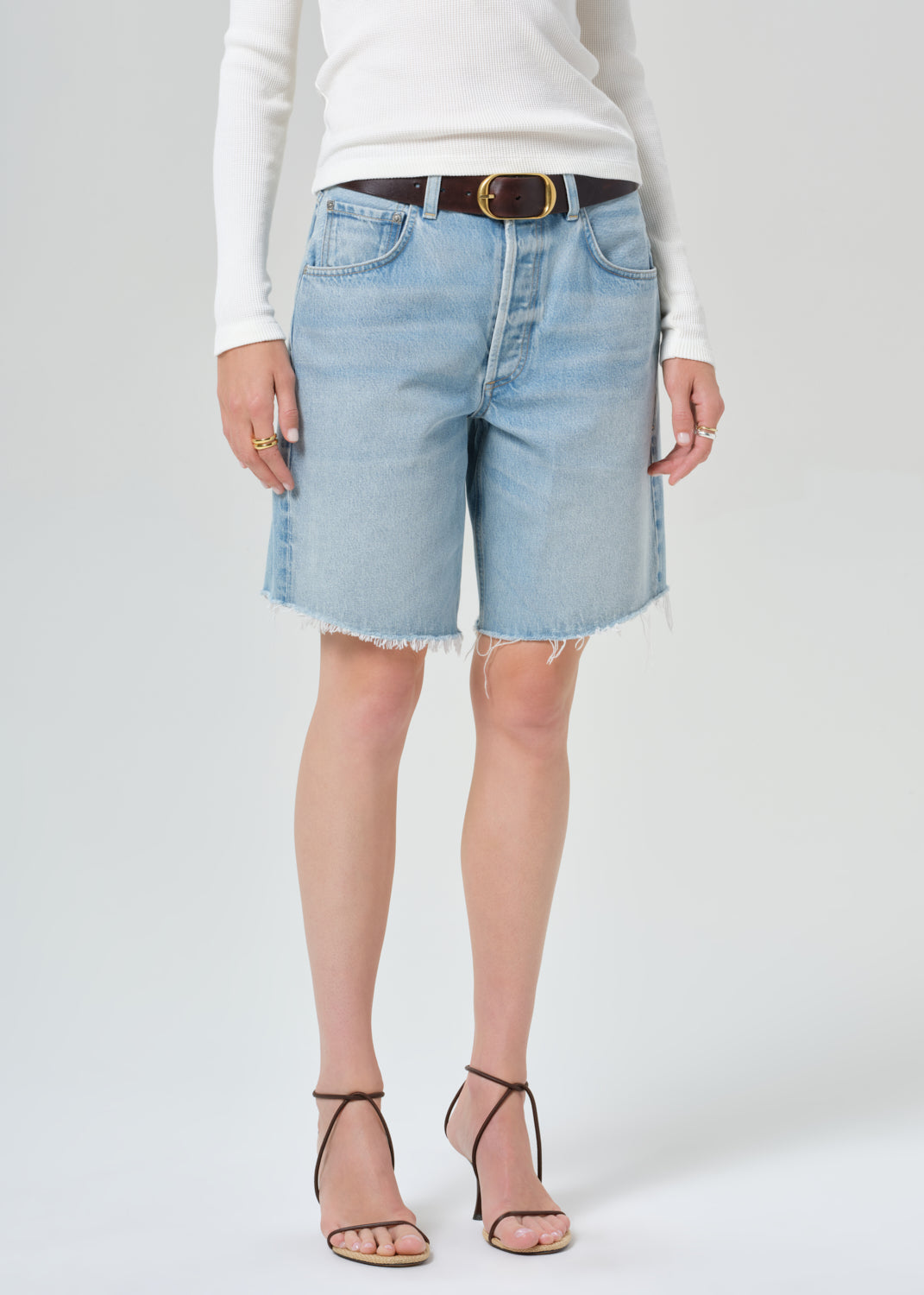 Person wearing a white long-sleeve shirt and light blue denim shorts on a plain background