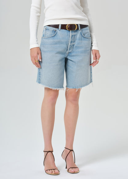 Person wearing a white long-sleeve shirt and light blue denim shorts on a plain background