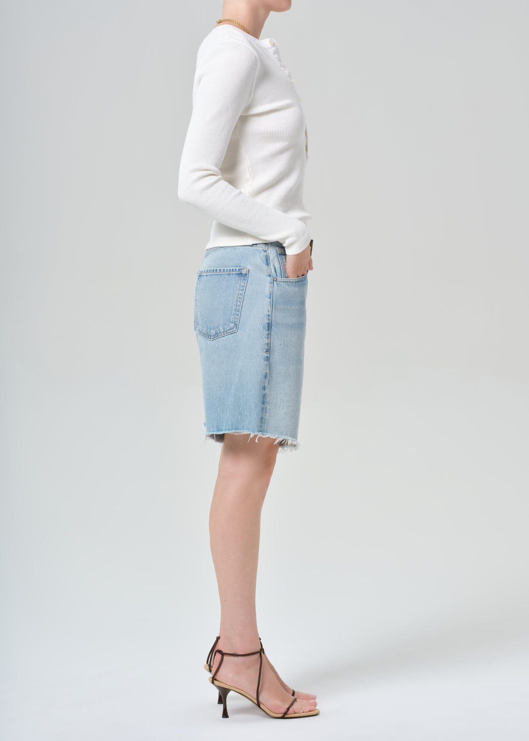 Person wearing a white long-sleeve shirt and light blue denim shorts on a plain background