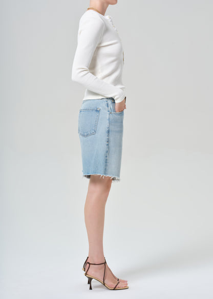 Person wearing a white long-sleeve shirt and light blue denim shorts on a plain background