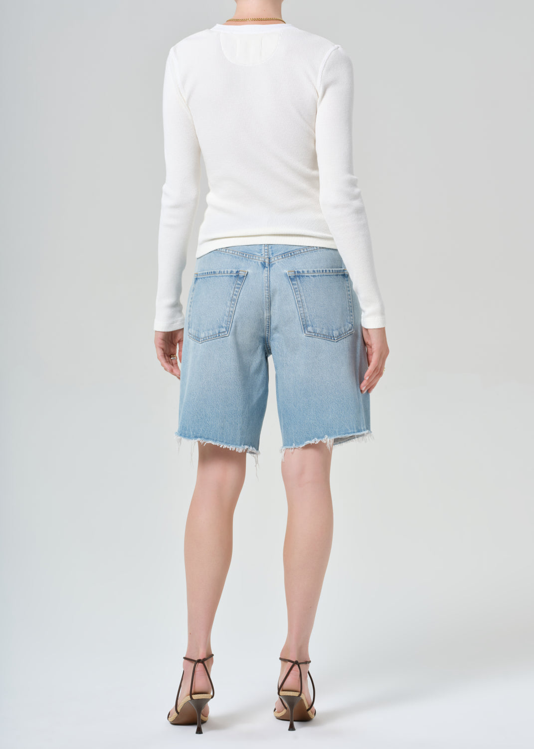 Person wearing a white long-sleeve shirt and light blue denim shorts on a plain background