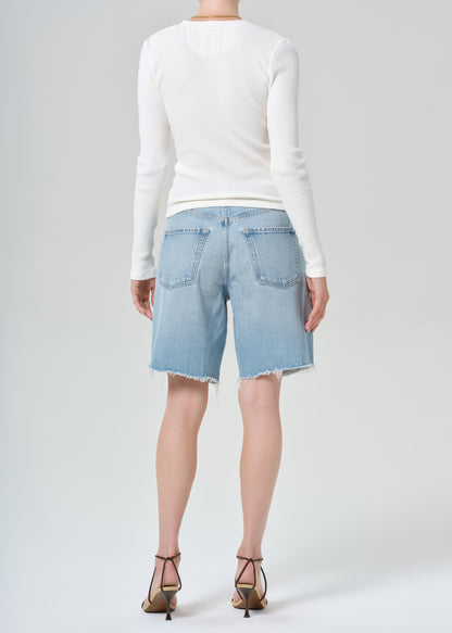 Person wearing a white long-sleeve shirt and light blue denim shorts on a plain background