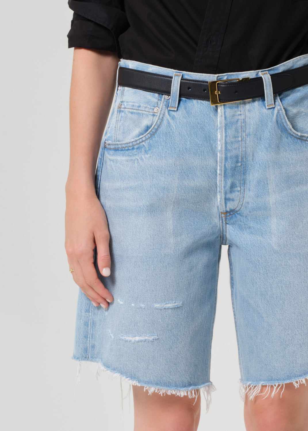 Person wearing a black shirt and light blue denim shorts on a grey background