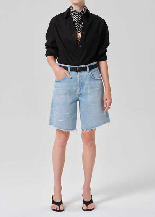 Person wearing a black shirt and light blue denim shorts on a grey background