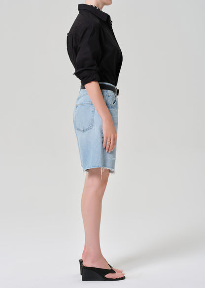 Person wearing a black shirt and light blue denim shorts on a grey background