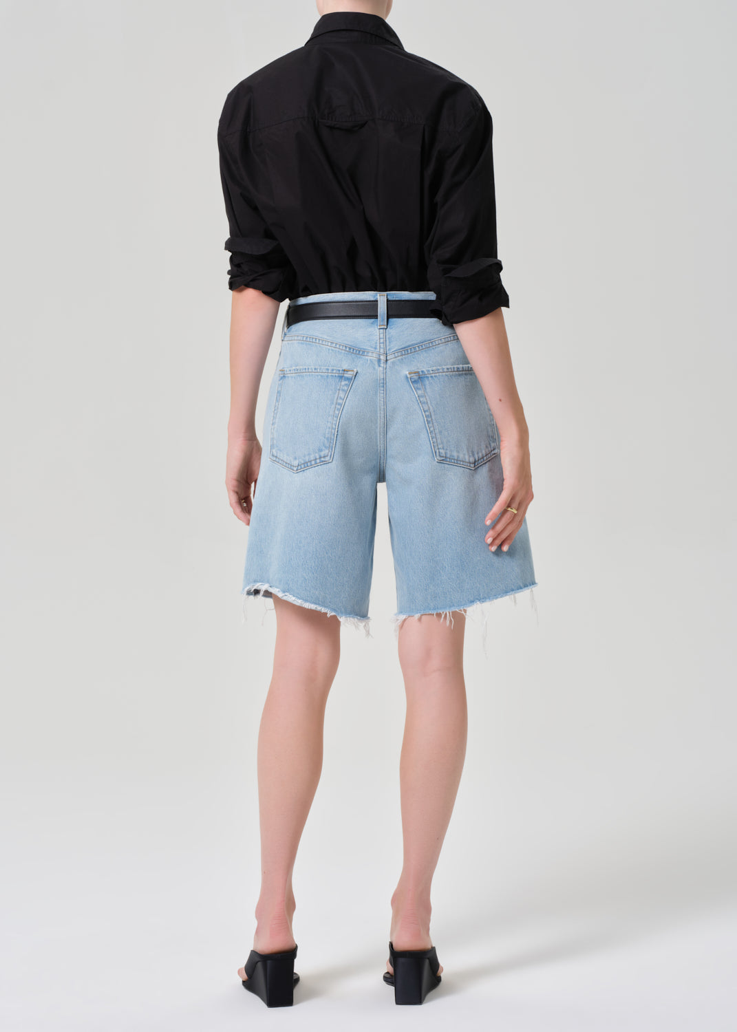 Person wearing a black shirt and light blue denim shorts on a grey background