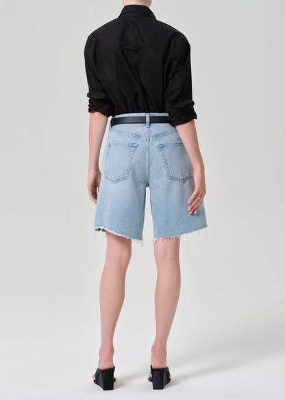 Person wearing a black shirt and light blue denim shorts on a grey background